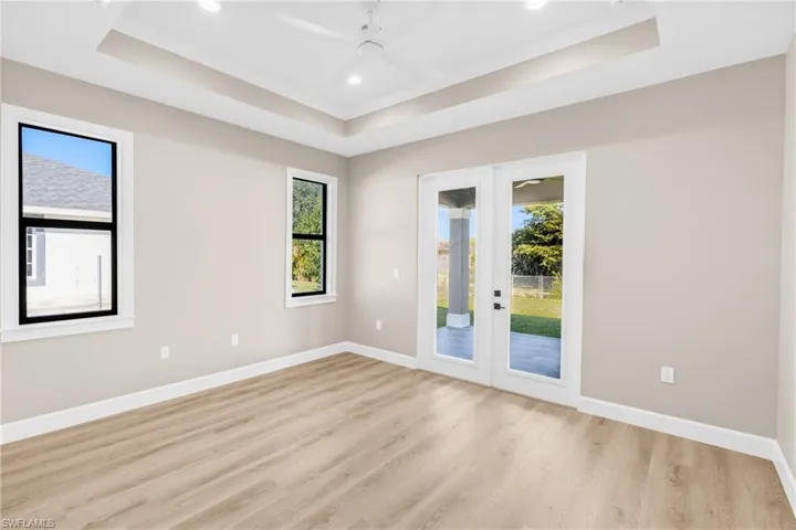 Unfurnished room featuring french doors, light wood-style flooring, recessed lighting, a ceiling fan, and a tray ceiling