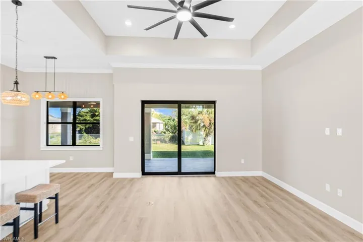 Unfurnished living room featuring a tray ceiling, light wood-style floors, ornamental molding, and a ceiling fan