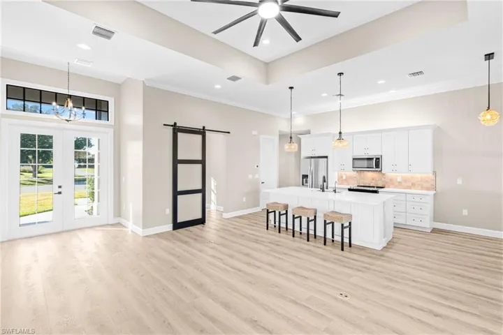 Kitchen with a barn door, white cabinetry, an island with sink, decorative light fixtures, and a breakfast bar area