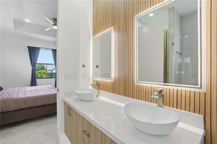 Ensuite bathroom featuring double vanity, a shower stall, wood walls, light marble finish floors, and ceiling fan