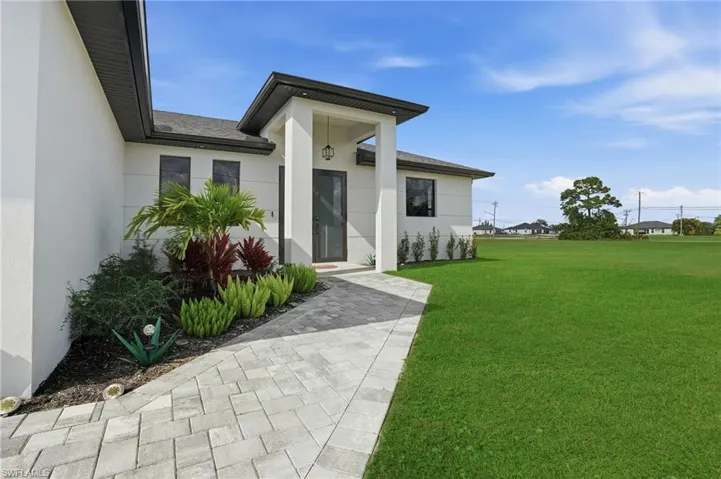 Doorway to property with a yard, stucco siding, and a shingled roof