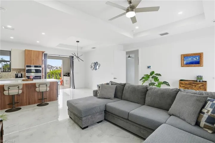 Living area featuring a tray ceiling, light marble finish floors, recessed lighting, ceiling fan, and a chandelier