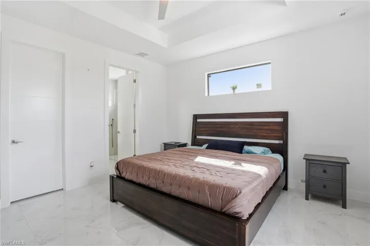 Bedroom featuring light marble finish flooring, a ceiling fan, a tray ceiling, and connected bathroom
