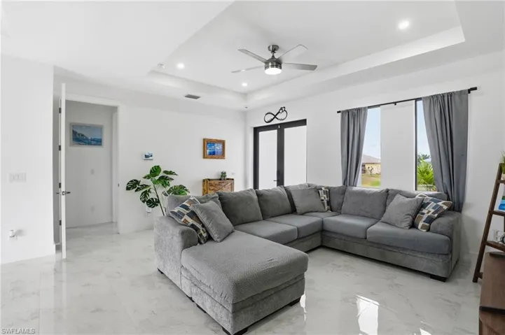 Living area featuring light marble finish floors, ceiling fan, a raised ceiling, and recessed lighting
