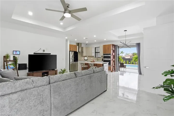 Living room featuring a raised ceiling, light marble finish floors, ceiling fan, a chandelier, and recessed lighting