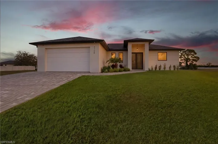 Prairie-style house with decorative driveway, stucco siding, a front yard, and a garage