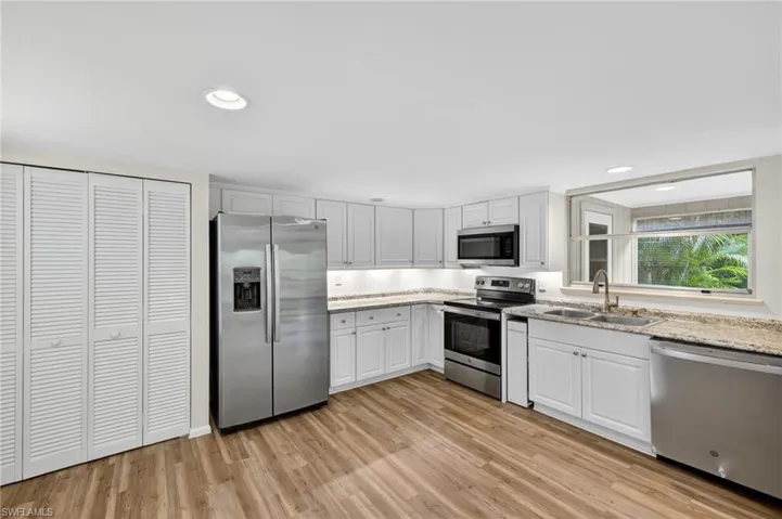 Kitchen with appliances with stainless steel finishes, light wood-style flooring, white cabinetry, recessed lighting, and light stone counters