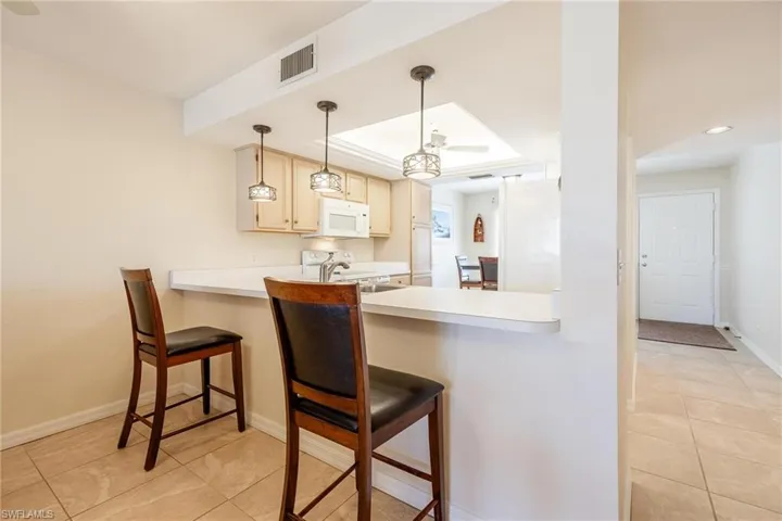 Kitchen featuring hanging light fixtures, light tile patterned floors, white appliances, and a breakfast bar
