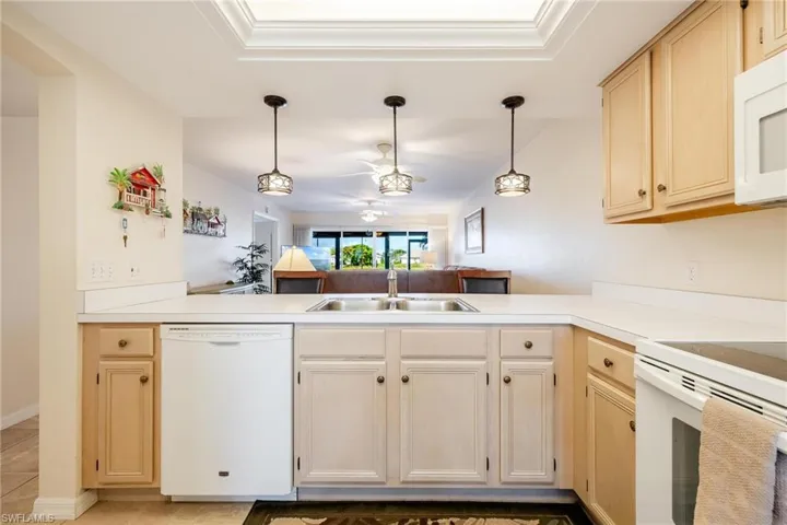 Kitchen with kitchen peninsula, sink, decorative light fixtures, and white appliances