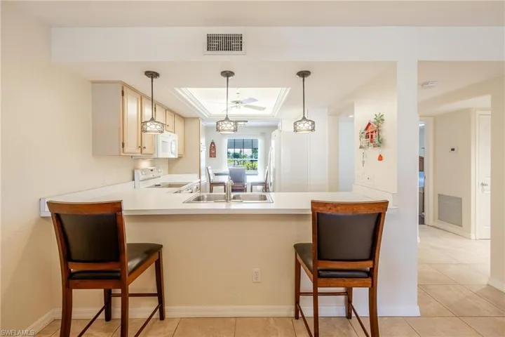 Kitchen with white appliances, sink, a raised ceiling, kitchen peninsula, and a kitchen breakfast bar
