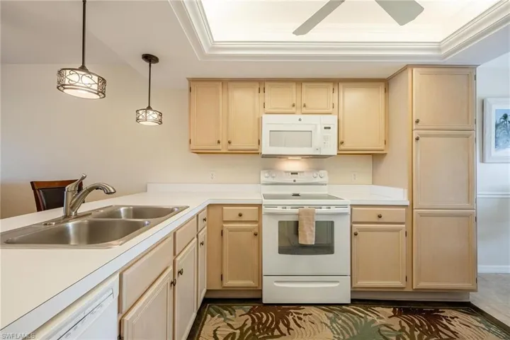 Kitchen with ornamental molding, white appliances, light brown cabinetry, sink, and hanging light fixtures