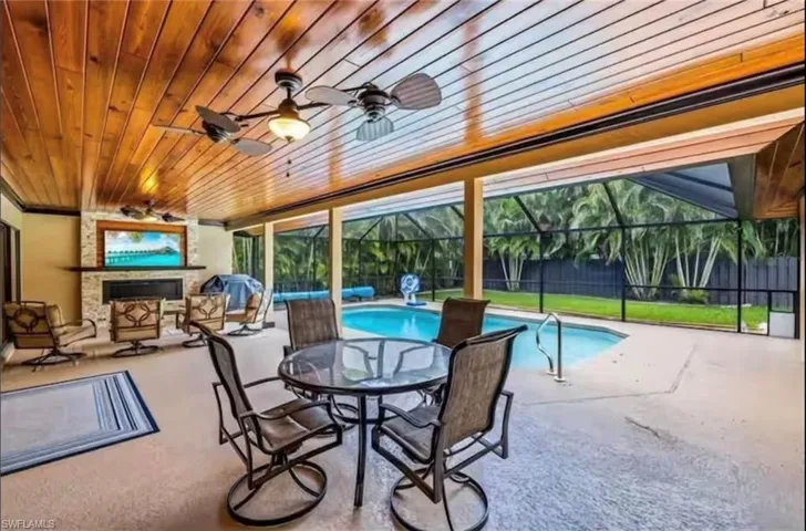 View of pool with glass enclosure, ceiling fan, a fireplace, and a patio area