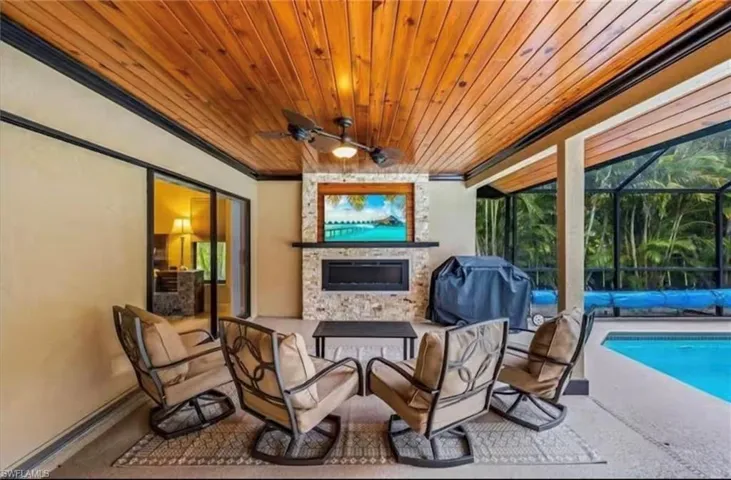 View of patio featuring grilling area, ceiling fan, a large fireplace, and glass enclosure