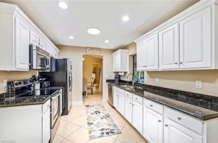 Kitchen with stainless steel appliances, sink, light tile patterned floors, dark stone countertops, and white cabinets