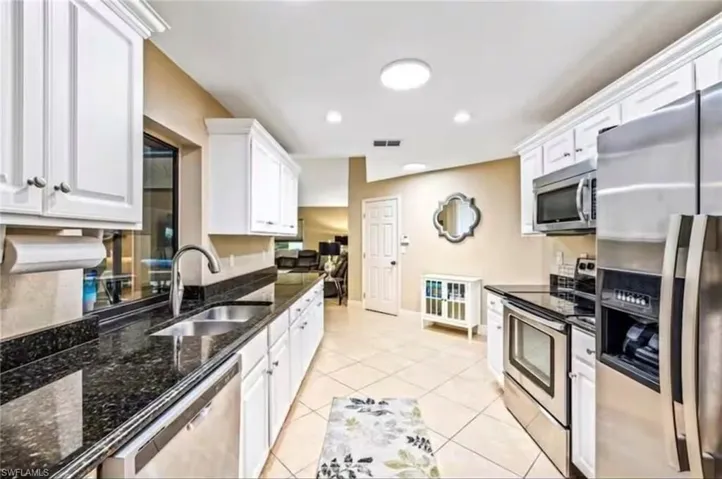 Kitchen with white cabinetry, sink, stainless steel appliances, dark stone counters, and light tile patterned floors