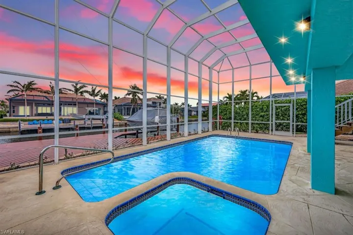 Pool at dusk with an in ground hot tub, glass enclosure, and a patio area
