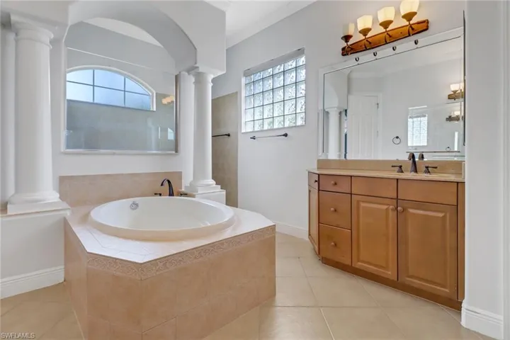 Bathroom with ornate columns, walk-in shower, a relaxing soaking tub, vanity & tile flooring