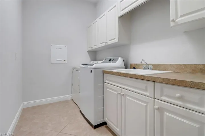Laundry room featuring light tile floors, cabinetry, laundry sink, washer and dryer