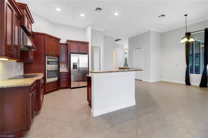 Kitchen featuring decorative backsplash, granite countertops, cooktop with hood, light tile floors & stainless steel appliances