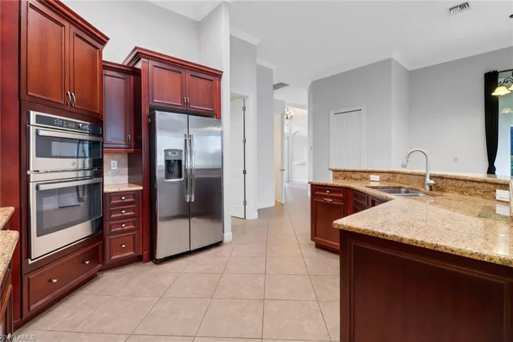 Kitchen with appliances with stainless steel finishes, light tile patterned floors, light stone counters, and sink