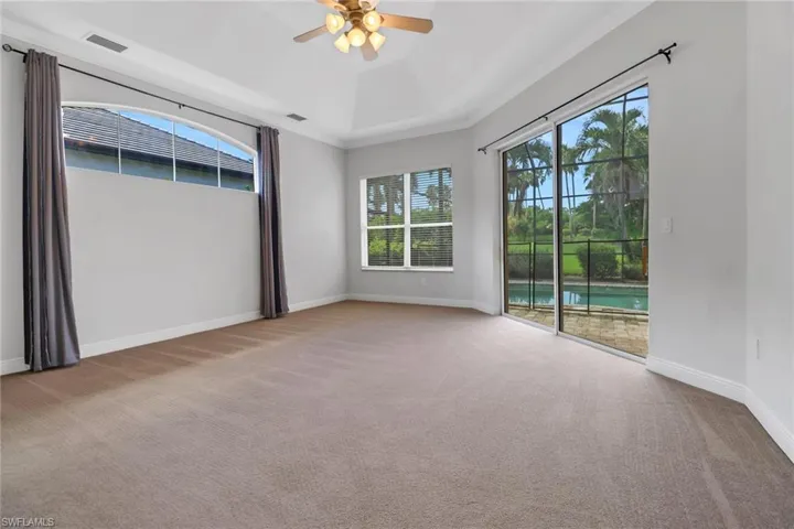 Carpeted main bedroom with ceiling fan, tray ceiling & sliding glass door leading to the screen lanai