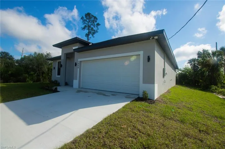 View of front of house with a front yard, driveway, an attached garage, and stucco siding