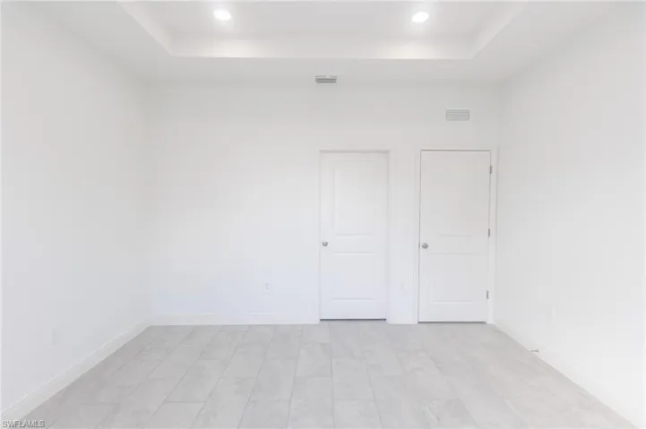 Master bedroom with a raised ceiling, visible vents, baseboards, and tile floors.