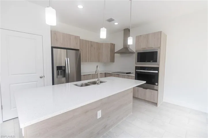 Kitchen with wall chimney range hood, modern cabinets, appliances with stainless steel finishes, and light brown cabinetry