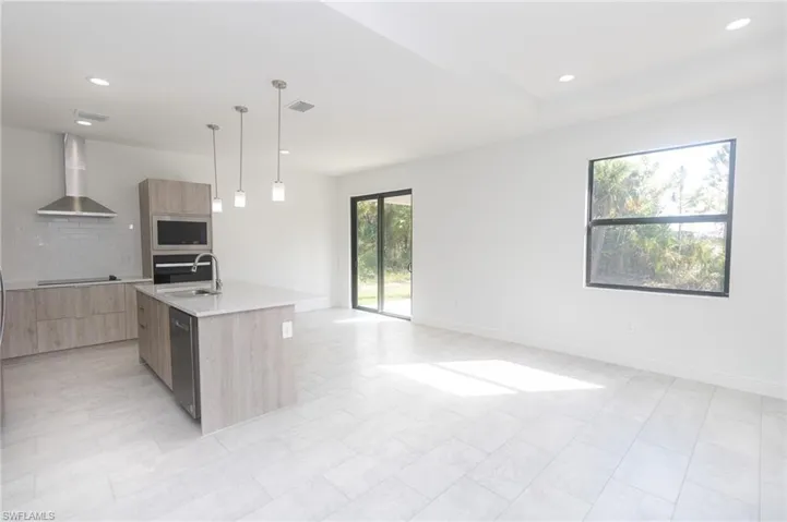 Kitchen with wall chimney range hood, modern cabinets, appliances with stainless steel finishes, and light brown cabinetry