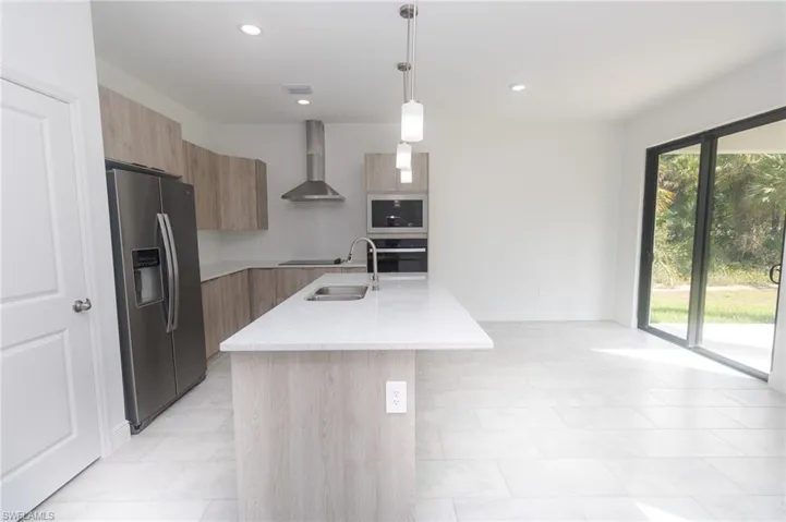 Kitchen with wall chimney range hood, modern cabinets, appliances with stainless steel finishes, and light brown cabinetry