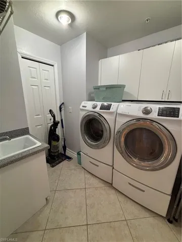 Dedicated laundry area featuring tile flooring, white cabinetry, a utility sink with a speckled countertop, and a double-door utility closet