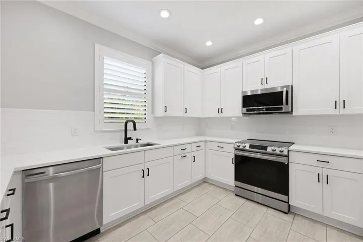 Kitchen featuring ornamental molding, sink, appliances with stainless steel finishes, and white cabinets