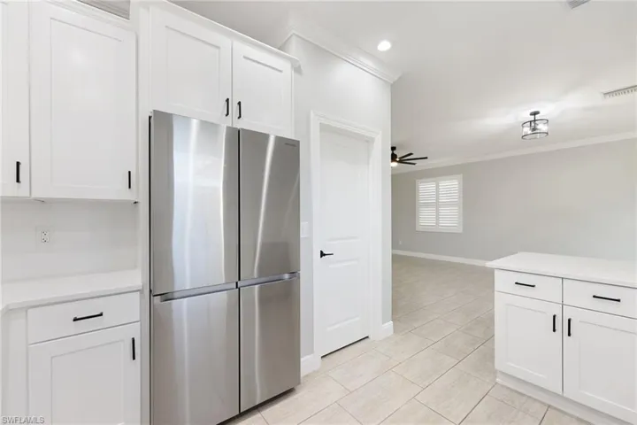 Kitchen featuring ceiling fan, stainless steel refrigerator, ornamental molding, and white cabinets