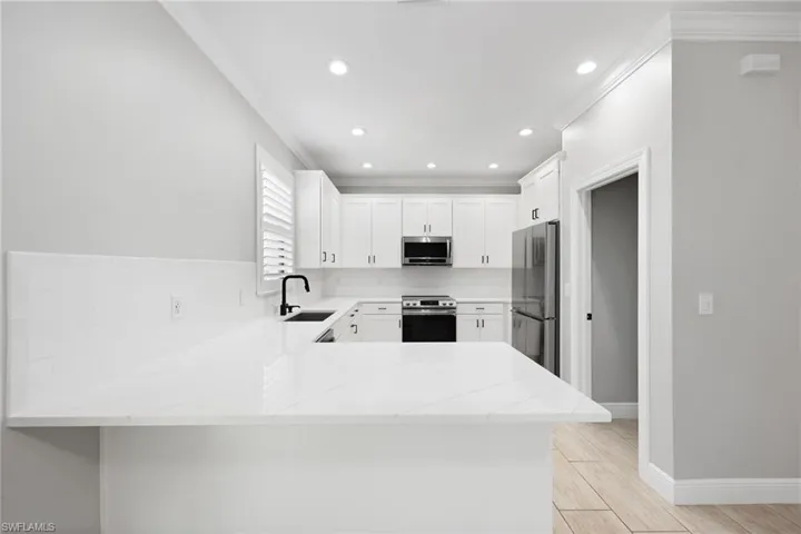 Kitchen with kitchen peninsula, stainless steel appliances, sink, white cabinetry, and light stone counters
