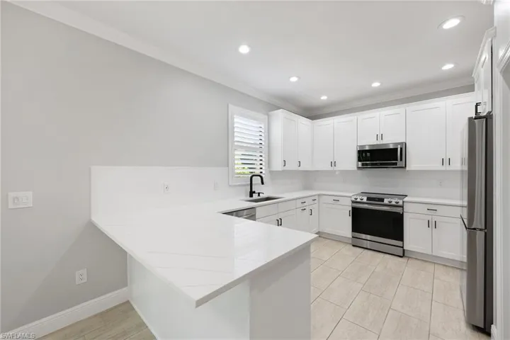 Kitchen with kitchen peninsula, light stone counters, appliances with stainless steel finishes, white cabinetry, and sink