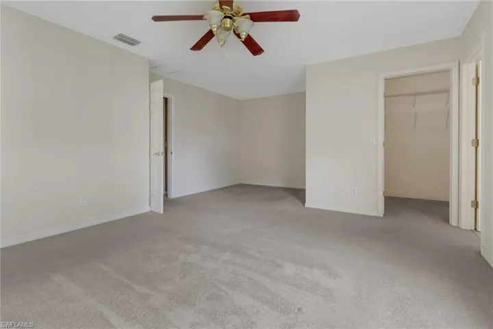Unfurnished bedroom featuring a spacious closet, light colored carpet, and ceiling fan