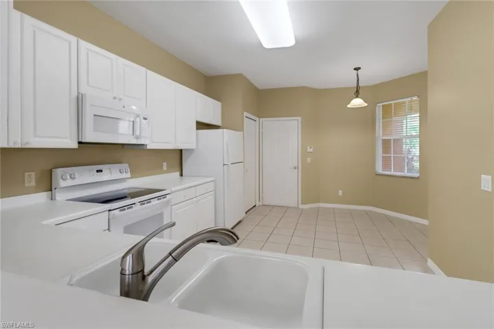 Kitchen featuring white appliances, white cabinets, light countertops, hanging light fixtures, and light tile patterned floors