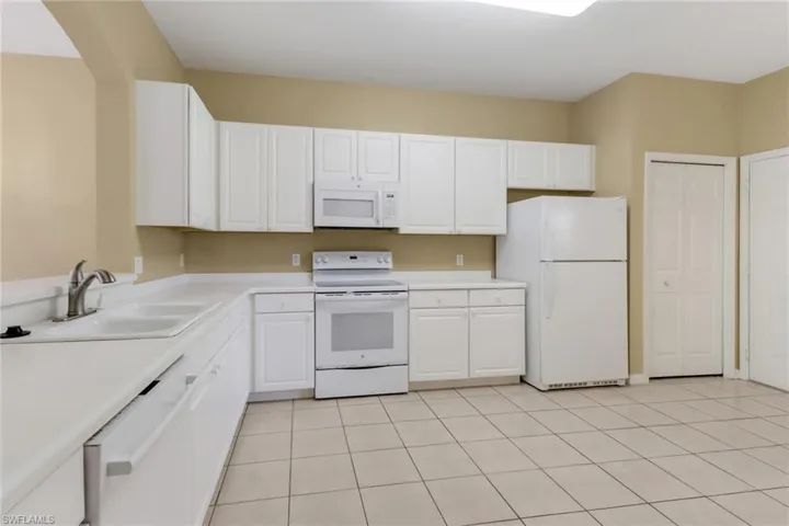 Kitchen featuring white appliances, light countertops, white cabinetry, and light tile patterned floors