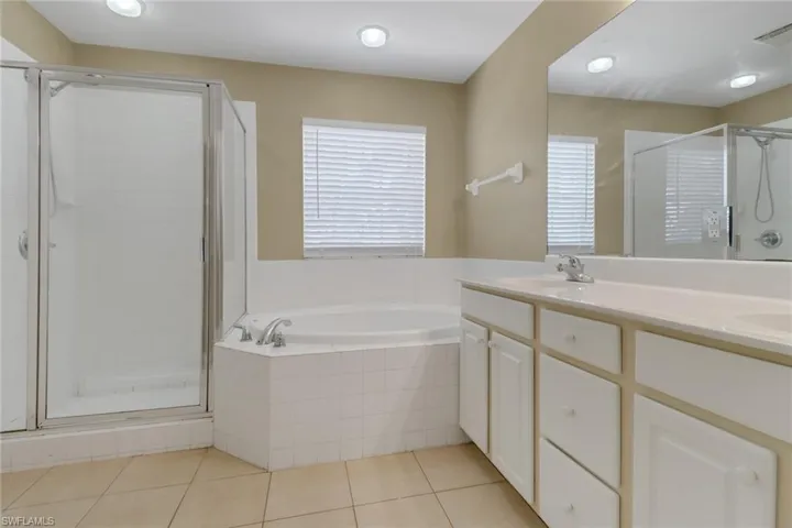 Full bath with a bath, a shower stall, double vanity, light tile patterned flooring, and healthy amount of natural light