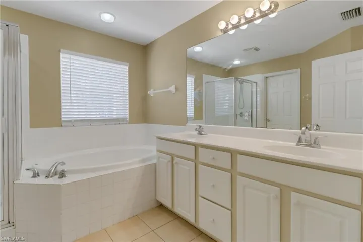 Bathroom with a shower stall, double vanity, a bath, and light tile patterned floors