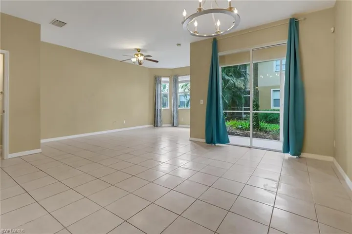 Empty room featuring a chandelier, light tile patterned flooring, and a ceiling fan