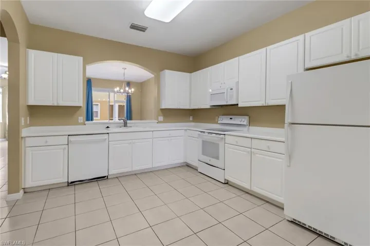 Kitchen featuring white appliances, a chandelier, arched walkways, white cabinets, and light countertops