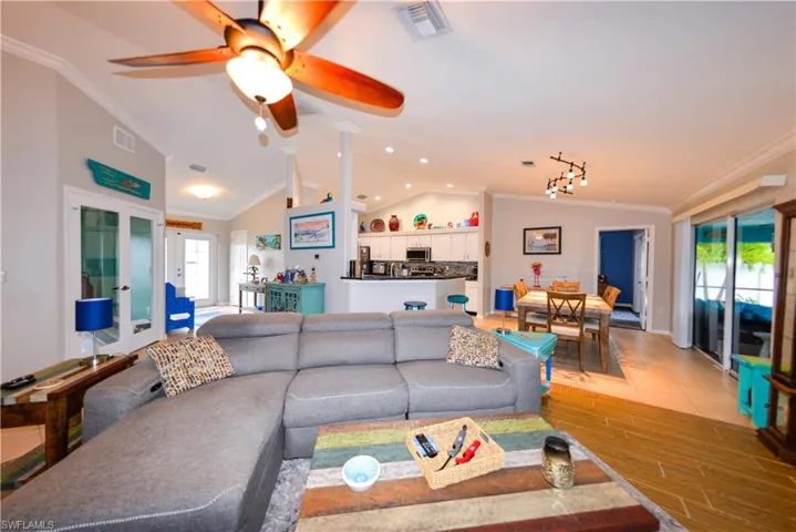 Living room featuring vaulted ceiling, ceiling fan, rail lighting, and crown molding