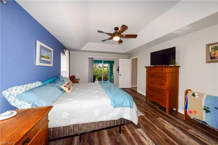 Bedroom with access to outside, a tray ceiling, wood-style floors, and ceiling fan
