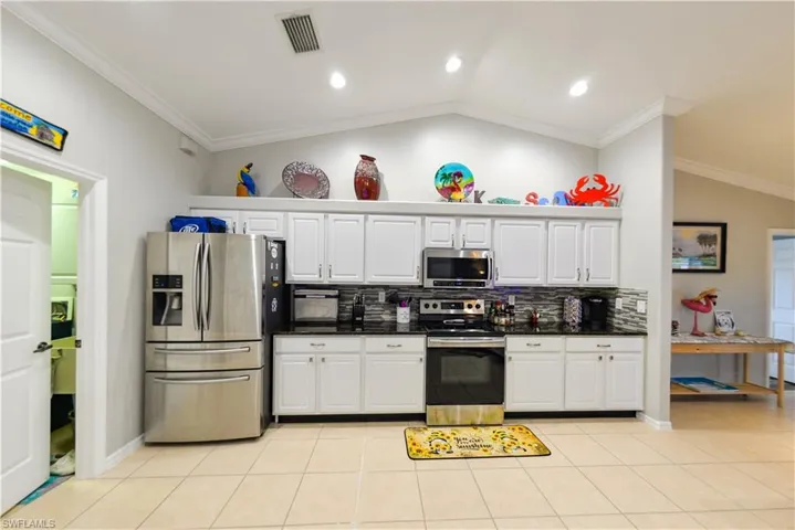 Kitchen featuring light tile floors, white cabinetry, vaulted ceiling, and stainless steel appliances