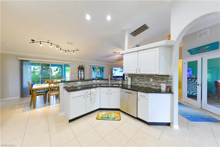 Kitchen featuring white cabinetry, kitchen peninsula, track lighting, light tile flooring, and dishwasher