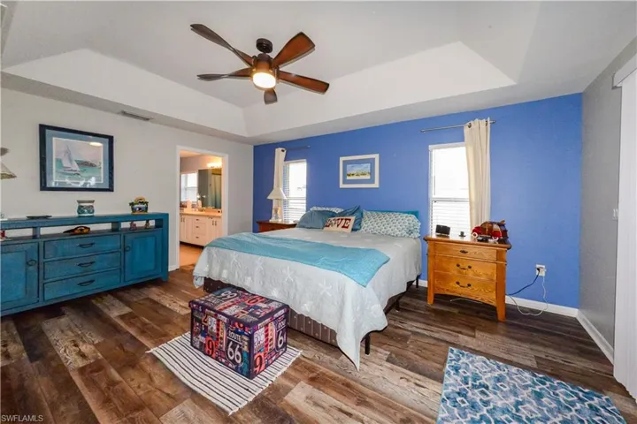 Primary Bedroom with ensuite bath, ceiling fan, a tray ceiling, and luxury vinyl wood-style flooring