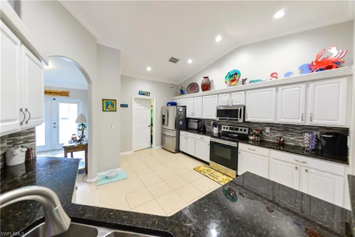 Kitchen with white cabinetry, lofted ceiling, appliances with stainless steel finishes, tasteful backsplash, and light tile floors