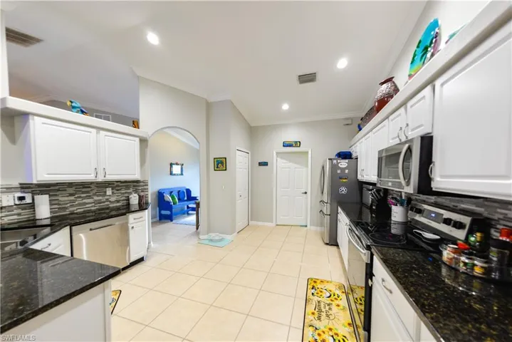 Kitchen with dark stone counters, light tile flooring, backsplash, white cabinets, and appliances with stainless steel finishes