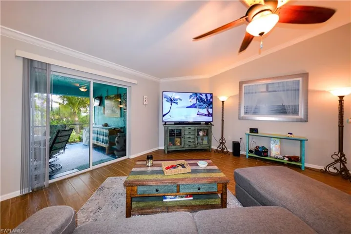 Living room featuring vaulted ceiling, luxury vinyl tile flooring, ceiling fan, and crown molding